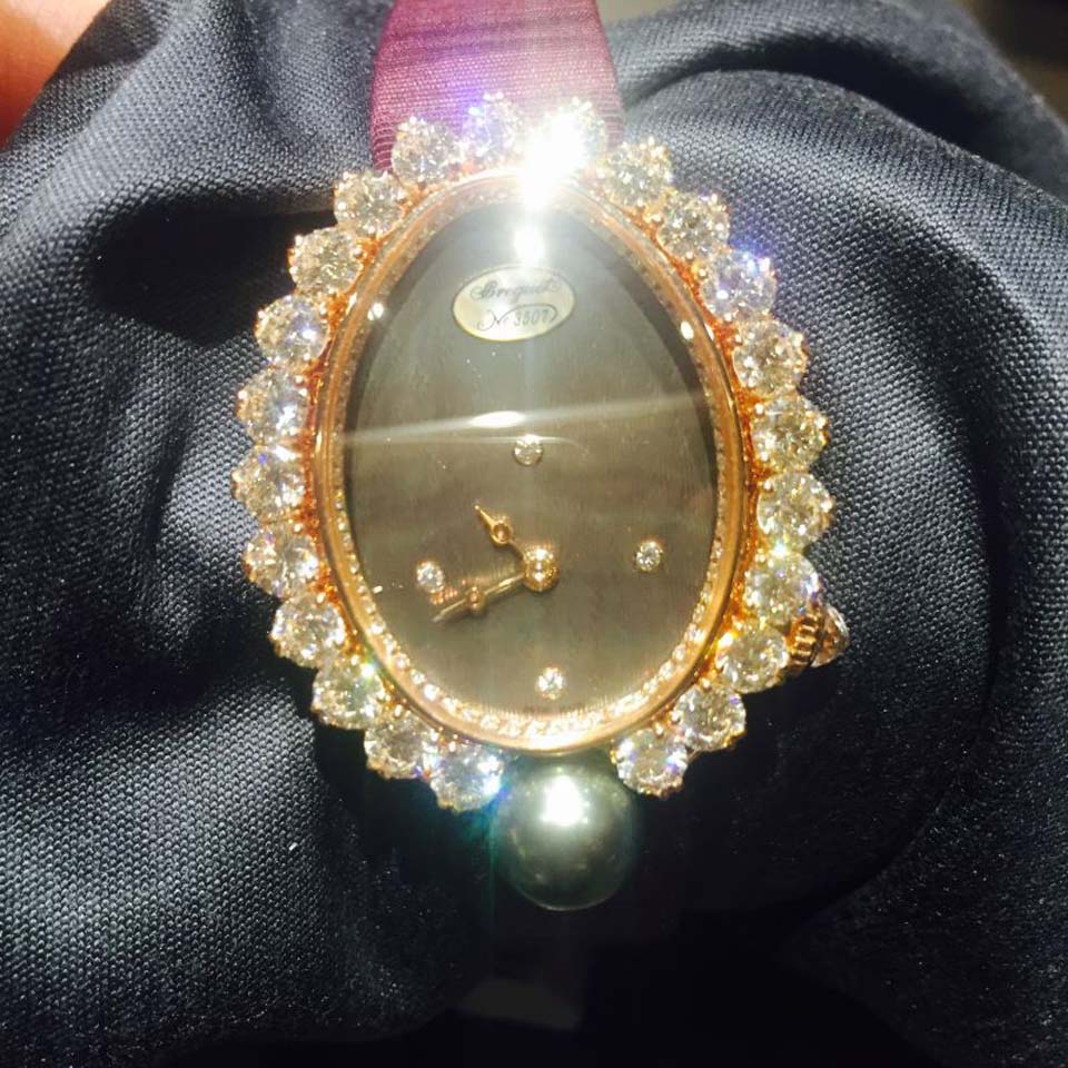 宝玑Perles Imperiales简直闪耀到无法对焦！延续了法国宫廷气质，表壳为18K白金，鹅卵形表壳，外缘镶嵌24颗明亮式切割钻石（约0.24克拉）。四周镶嵌23颗明亮式切割钻石（约4.12克拉）和一颗日本Akoya 海水珍珠。表壳凸缘镶嵌66颗明亮式切割钻石（约0.13克拉）。棘爪下方底座上镶有15颗明亮式切割钻石（约0.93克拉）。表冠镶嵌一颗梨形钻石（约0.28克拉）。蓝宝石水晶底盖。尺寸：34.4 x 28.7毫米。表盘为玑镂刻花珍珠母贝。12点位置镶嵌宝玑铭牌。偏心小时刻度环，3点、6点、9点和12点位置设有钻石时标。宝玑经典针尖镂空式蓝钢指针。