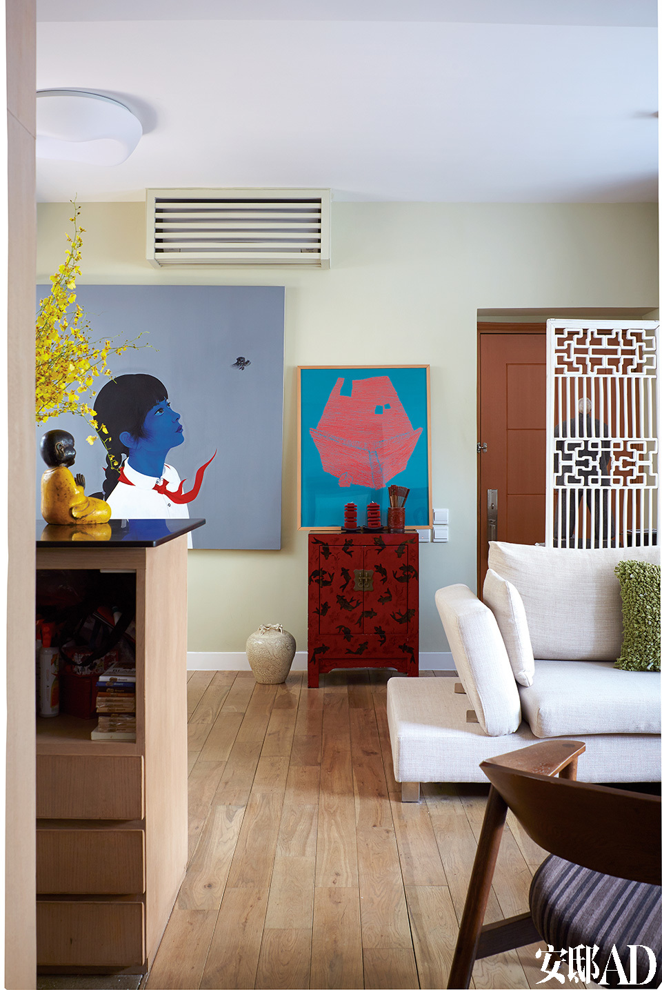起居空间里结合了当代艺术、现代家具和一些中式元素，完全是东方遇上西方的一场精彩对话！绿玉色的墙上挂着一幅以中国小女孩为主题的油画，是由中国艺术家房辉创作的。白色矮沙发与红色中式边柜，再加上一抹亮黄色，整个起居室流露出轻松又活力十 足的气氛。