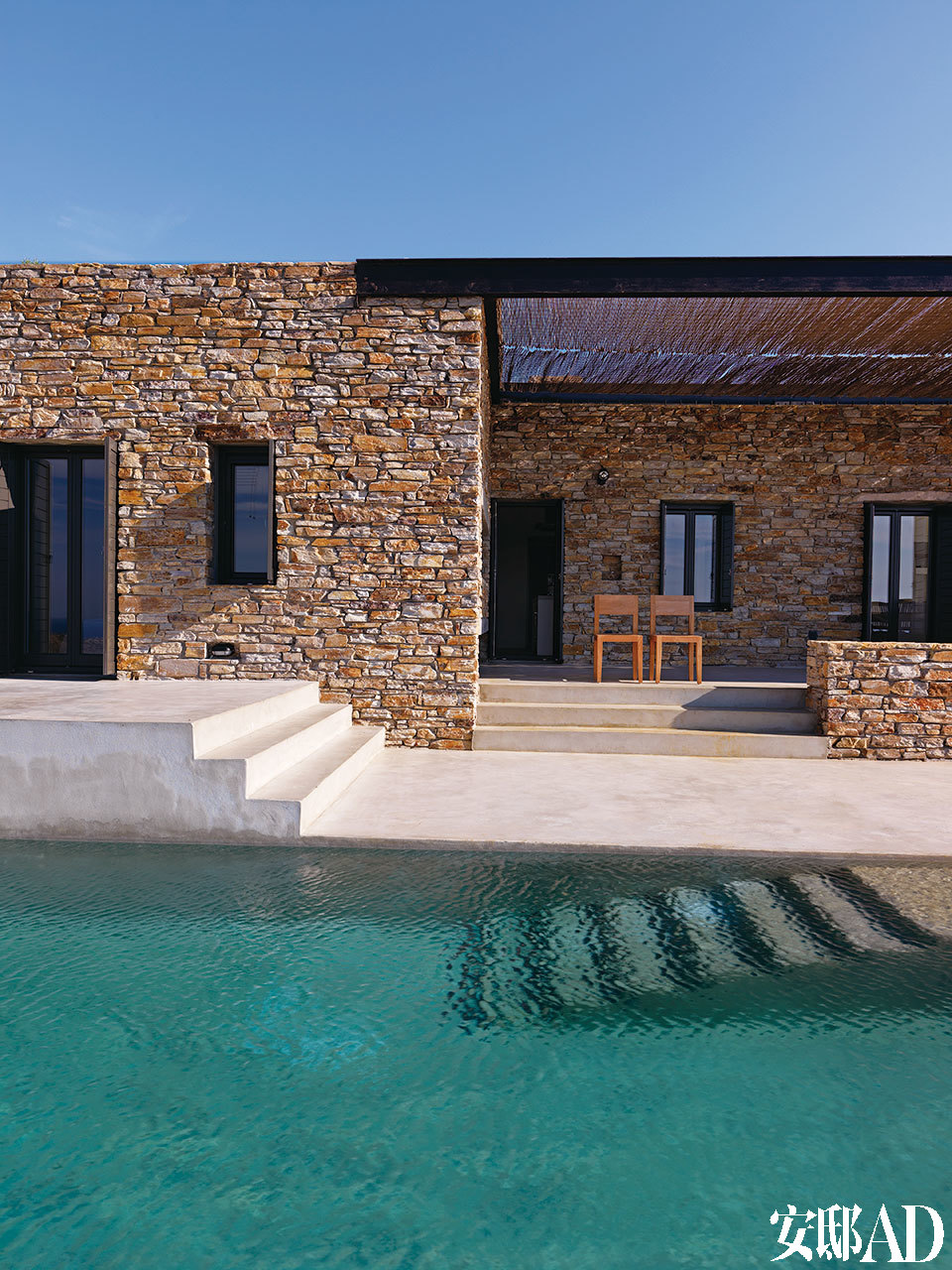 泳池一侧看向房屋，石砌的外墙显得粗朴自然。