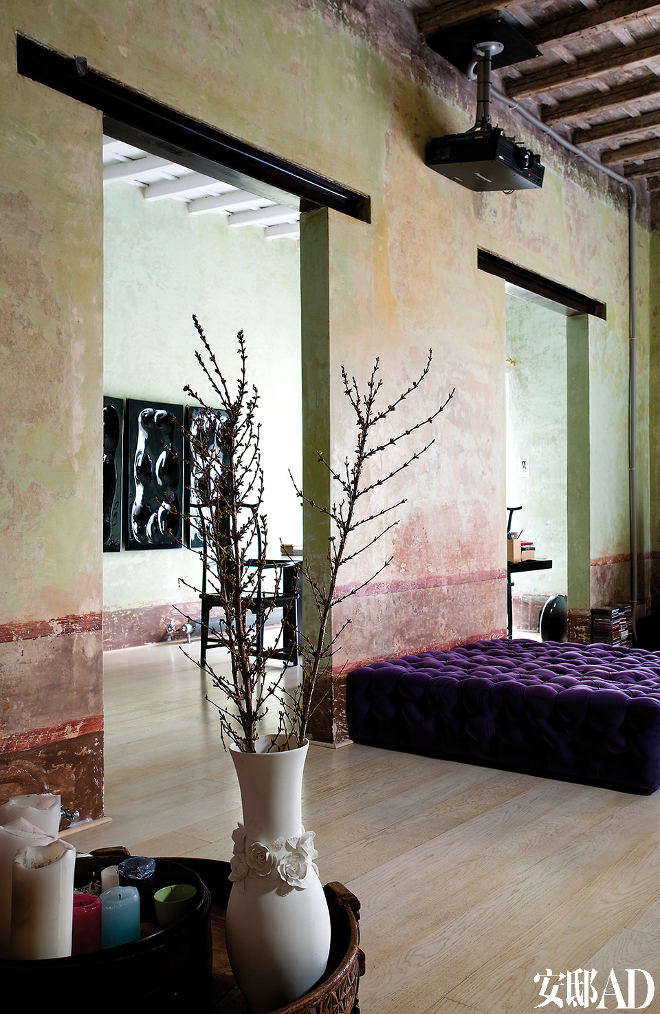 从起居室能看到书房一景。La Michetta紫色绒面沙发由Gaetano Pesce为Meritalia设计。复古木桌上摆放着蜡烛和白色陶花瓶，里面的植物营造出了中国蜡梅的效果。