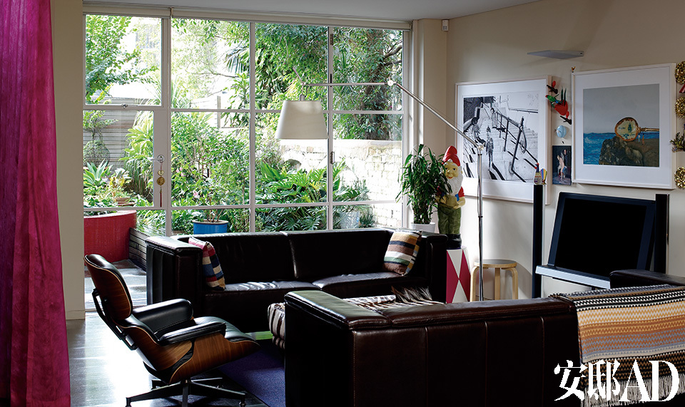 房屋改造的重点之一，就是尽可能多地打开客厅与花园之间的墙体面积，将阳光与绿色生动地引入室内。钢制细框玻璃窗将葳蕤的花园最大限度地引进客厅中，两只Brescia Furniture的双人皮沙发上搭配了Missoni的彩色靠垫，旁边立着一座Artemide品牌的Tolomeo地灯以及Herman Miller出品的Eames躺椅，上方的壁灯来自Targetti Squadra。墙上的三幅艺术品从左起分别是Matt Coyle的“Worry Dolls Setting Out”、Shonah Trescott的“Susanna and the Elders No.12”，以及Elaine Campaner的“Ballina”。