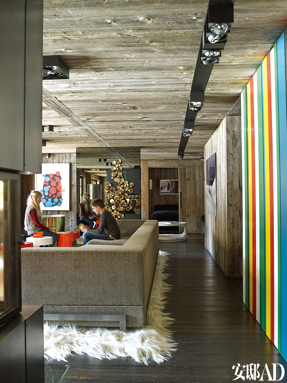 客厅中宽大的沙发是设计师Thierry Lemaire为这个空间特别定制的，漆面茶几也是Thierry的设计。木墙上油画的作者是José Pedro Croft，一旁在形状上与其相呼应的镜面艺术品由Curtis Gere创作，天花板照明装置使用了Modular。