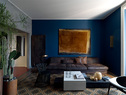 老旧的地砖，以质朴、静默的色调，主导着客厅。宽大的棕色皮质沙发占据了几乎一整侧的位置，沙发上方深蓝色墙面上悬挂着的艺术品，与一旁硕大的金属落地阅读灯，都使用了相近颜色。暖气被藏在一块巨大的金属板后面，与室内陈设所使用的基调和谐地相处。